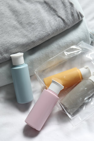Cosmetic travel kit. Plastic bag with small containers of personal care products and stack of clothes on bedの写真素材