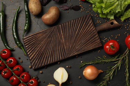 Cooking concept. Wooden cutting board and different products on black table, flat lay