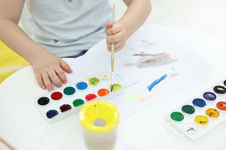 Little boy painting with brush and watercolor at white table, closeupの写真素材