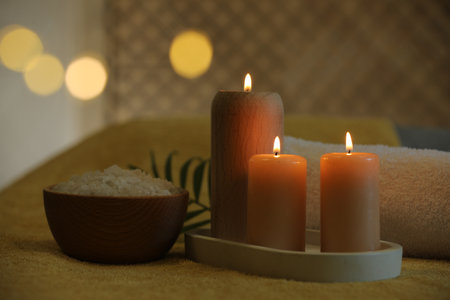 Spa composition. Burning candles, sea salt and towel on soft yellow surface