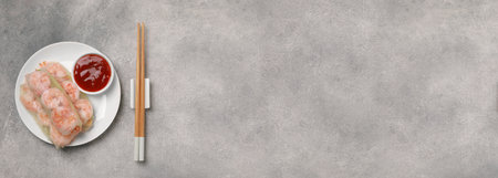 Delicious spring rolls with shrimps, sauce and chopsticks on gray table, top view. Banner design...