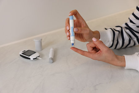Diabetes. Woman using lancet pen at light table, closeupの写真素材