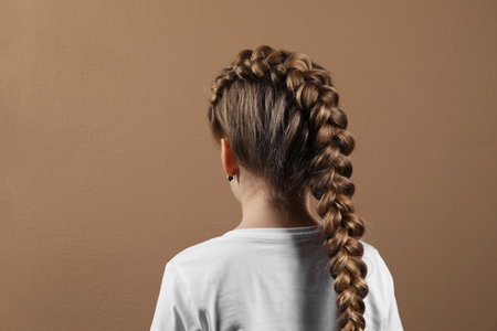 Little girl with braided hair on light brown background, back view