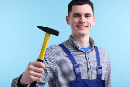 Professional repairman holding hammer on light blue backgroundの写真素材