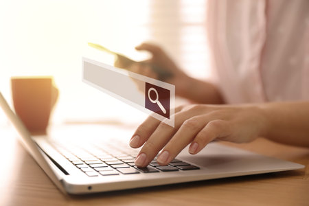 Search bar of website over laptop. Woman using computer at wooden table, closeupの写真素材