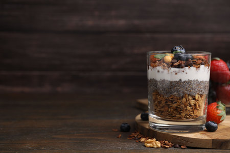 Tasty granola with berries, nuts, yogurt and chia seeds in glass on wooden table, space for textの写真素材
