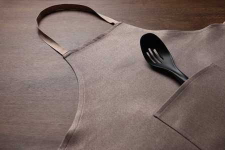 Stylish brown apron and slotted spoon on wooden table. Space for textの写真素材