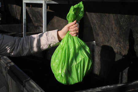 Woman throwing trash bag full of garbage in bin outdoors, closeup