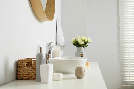 Vase with beautiful white roses and toiletries near sink in bathroomの写真素材