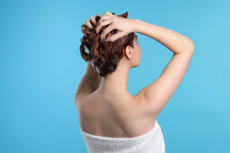 Young woman washing her hair with shampoo on light blue background, back viewの写真素材