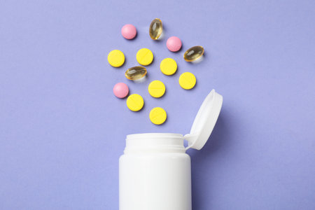 White bottle and different vitamin pills on violet background, top viewの写真素材