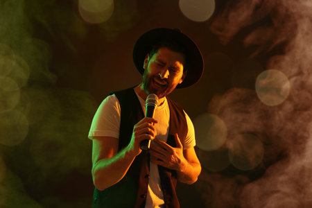 Handsome man with microphone singing on stage in color lighted smokeの写真素材