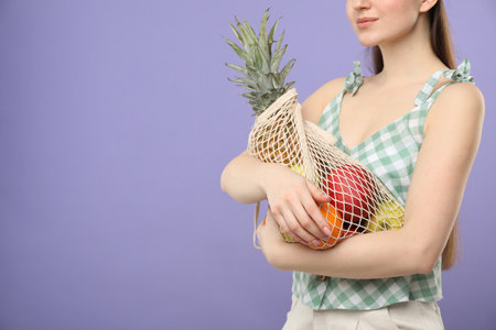 Woman with string bag of fresh fruits on violet background, closeup. Space for textの写真素材
