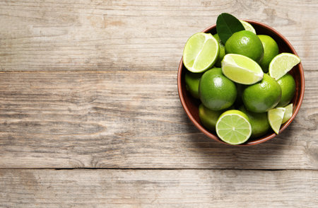 Tasty ripe limes in bowl on wooden table, top view. Space for textの写真素材