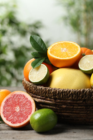Different fresh citrus fruits and leaves in wicker basket on wooden table against blurred background, closeupの写真素材