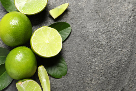Fresh ripe limes and leaves on gray table, top view. Space for text