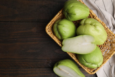 Cut and whole chayote in wicker basket on wooden table, flat lay. Space for textの写真素材