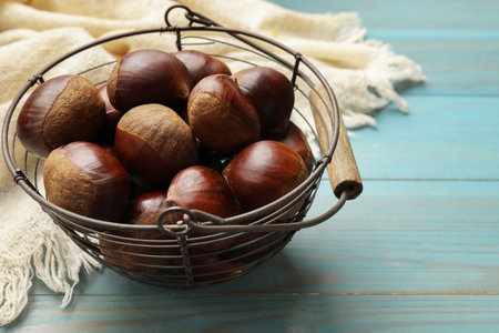 Roasted edible sweet chestnuts in metal basket on light blue wooden table, closeup. Space for textの写真素材