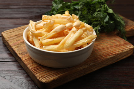 Delicious French fries with cheese sauce in bowl on wooden tableの写真素材