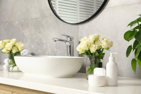 Beautiful roses and bath accessories near sink in bathroomの写真素材