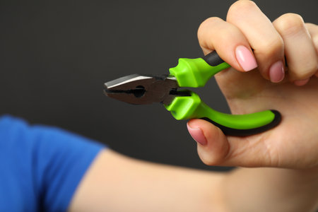 Woman with combination pliers on dark background, closeup. Space for textの写真素材