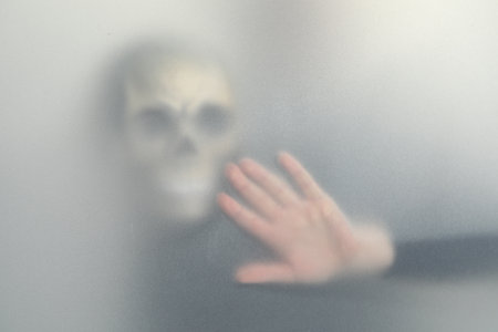 Silhouette of creepy ghost with skull behind cloth