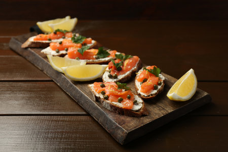 Tasty canapes with salmon, capers, lemon and cream cheese on wooden tableの写真素材