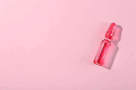 Glass ampoule with liquid on pink background, top view. Space for textの写真素材