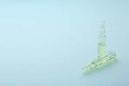 Glass ampoules with liquid on light blue background. Space for text