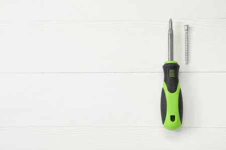 Screwdriver with green handle and screw on white wooden table, flat lay. Space for textの写真素材