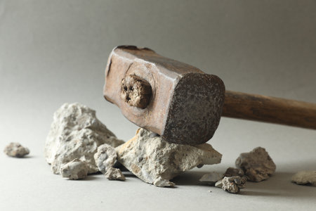 One sledgehammer and pieces of broken stones on gray background, closeup