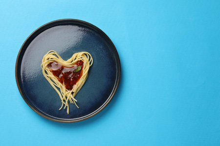 Heart made with spaghetti and sauce on light blue background, top view. Space for textの写真素材