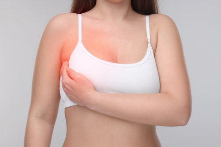 Young woman suffering from breast pain on light gray background, closeupの写真素材