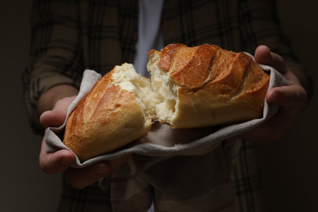Man breaking loaf of fresh bread on dark background, closeup