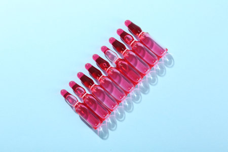 Glass ampoules with liquid on light blue background, top view