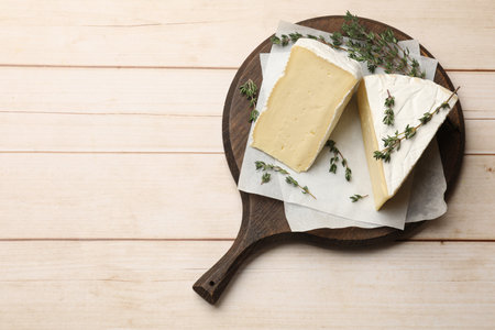 Board with pieces of tasty camembert cheese and thyme on light wooden table, top view. Space for textの写真素材