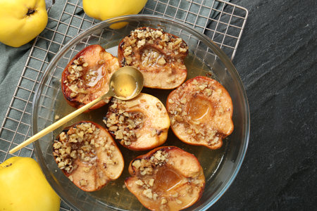 Tasty baked quinces with walnuts and honey in bowl on black table, flat layの写真素材