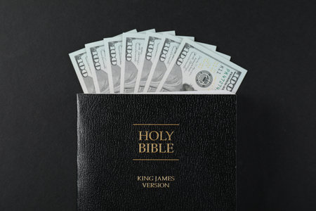 Holy Bible with money on black background, top view