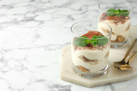 Delicious tiramisu in glasses, mint leaves and spoons on white marble table, space for textの写真素材
