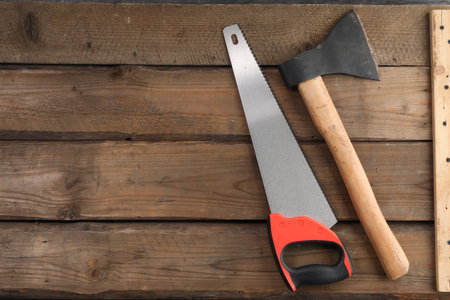 Saw with colorful handle and ax on wooden background, flat lay. Space for textの写真素材
