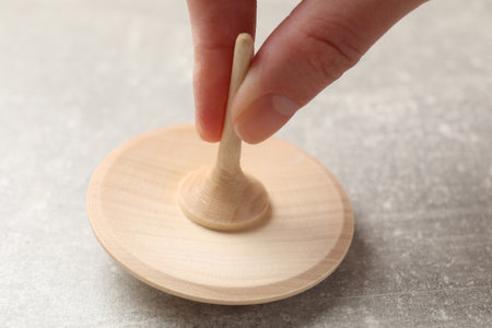 Woman playing with wooden spinning top at gray textured background, closeupの写真素材