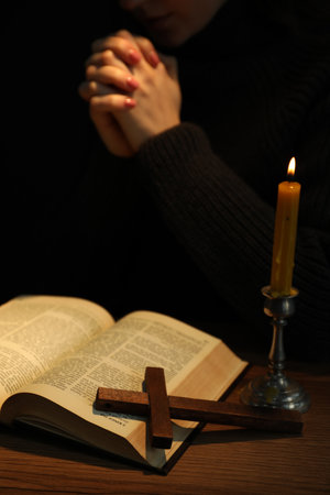 Woman praying at table with burning candle and Bible, closeup