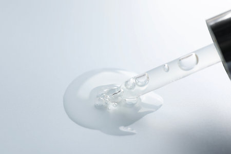 Dripping moisturizing serum from pipette on light gray background, closeup