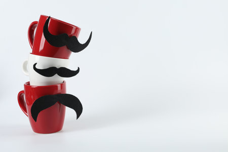 Cups with fake mustaches on light background, space for textの写真素材