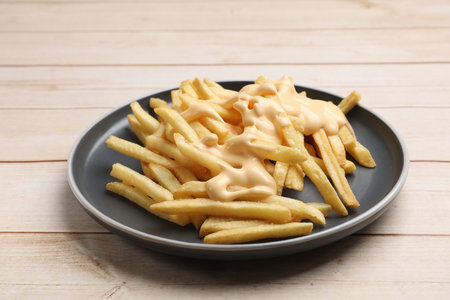 Delicious French fries with cheese sauce on wooden tableの写真素材