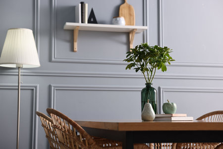 Vase with green branches, books and decor on wooden table in stylish dining roomの写真素材