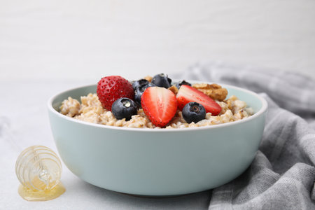 Tasty oatmeal with strawberries, blueberries and walnuts in bowl on gray table