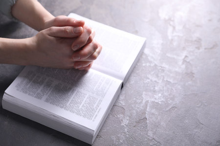 Religion. Christian woman praying over Bible at gray table, closeup. Space for textの写真素材