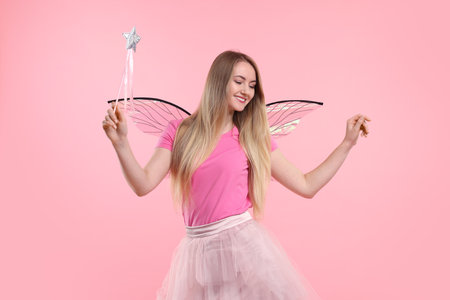 Beautiful girl in fairy costume with wings and magic wand on pink backgroundの写真素材