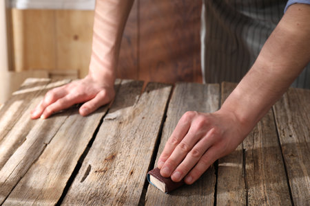 Man polishing wooden table with sandpaper indoors, closeupの写真素材